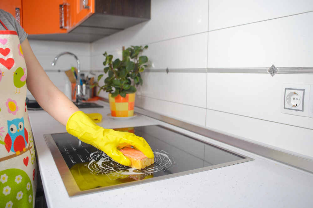 Blond Girl Yellow Gloves With Sponge Wiping Down Ceramic Electric Induction Stove Top Range Wide Angle Copy Space