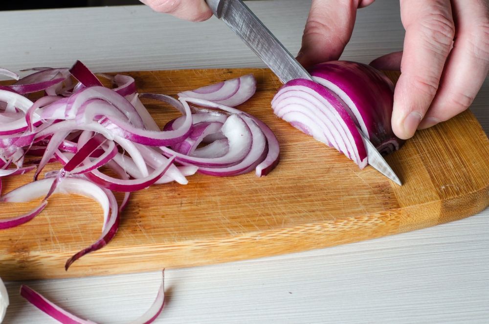 man-cuts-red-onions-wooden-chopping-board