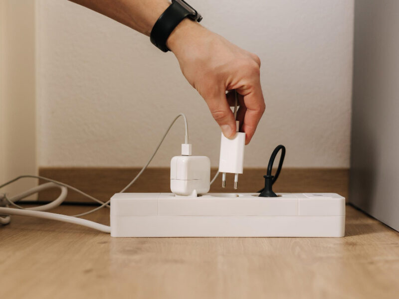 Human Hand Puts Charger Into Filled Extension Cord White Cable Connector Closeup Home Routine