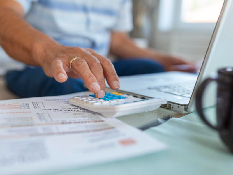 Serious Elder Senior Greyhaired Grandpa Using Calculator Counting Bank Loan Payment Holding Papers Home Focused Mature Old Man Doing Paperwork Calculating Bills Managing Finances Sit Sofa